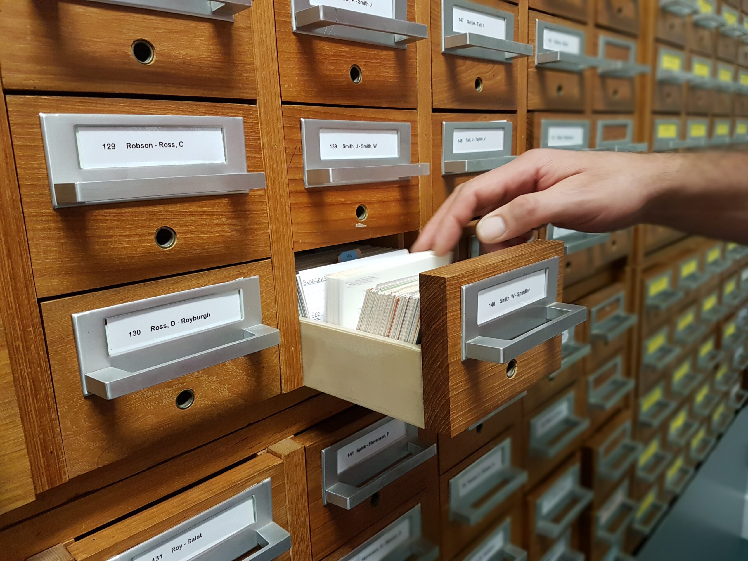 Landscape photo of a hand pulling folders from a metal filing cabinet drawer.